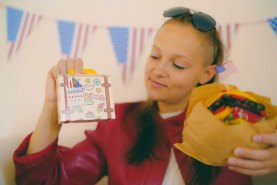 Kobieta trzymająca produkty od Rainbow Socks, skarpetki narodowościowe w walizce USA i skarpetkowy burger, pomysł na prezent