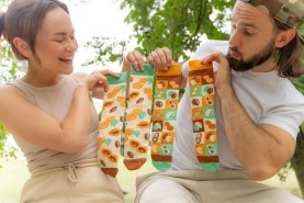 Mann und Frau halten bunte Baumwollsocken mit Erdnussmotiven, Socken in einer Dose, originelle Geschenkidee