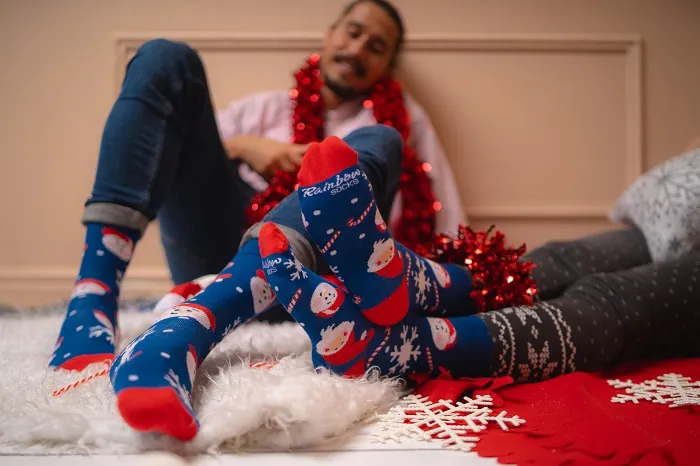 Man and woman in navy blue Christmas socks with snowmen and Santas.