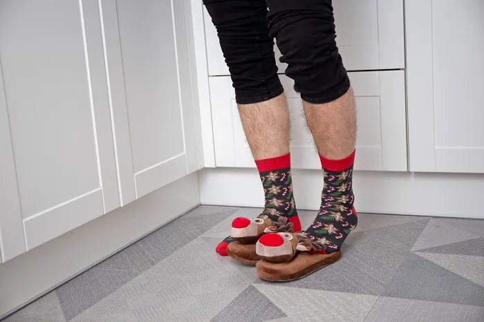Man wearing brown Christmas socks and reindeer slippers.