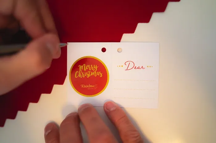 Someone filling out a greeting card attached to Christmas socks in a bauble from Rainbow Socks.