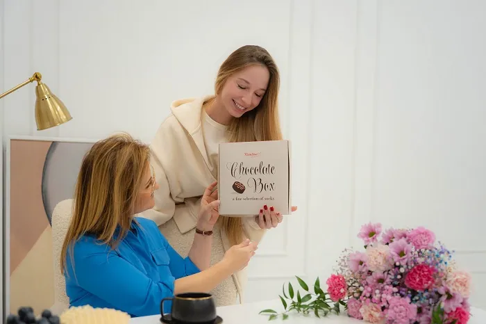 Woman handing socks in a box that looks like a box of chocolates as a Mother's Day gift to mother-in-law.