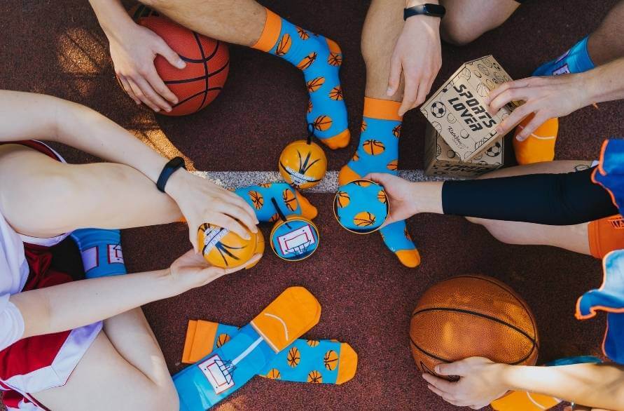 A group of people sitting on a basketball court wearing the Rainbow Socks Basketball socks.