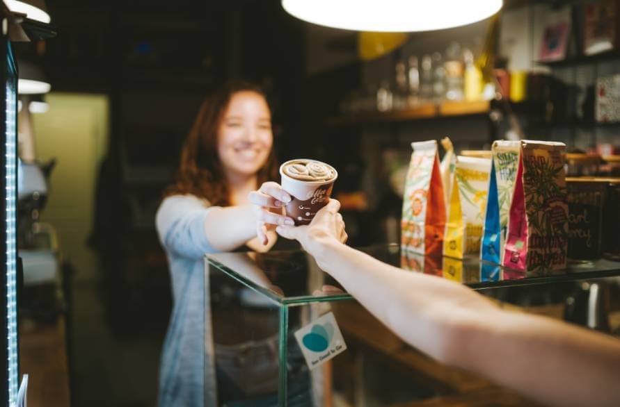 Kobieta w kawiarni odbiera od baristy kubek z kawowymi skarpetkami Rainbow