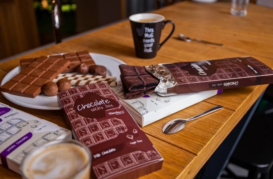 Chocolate bars, a cup of coffee and Rainbow Chocolate Socks on a table.   