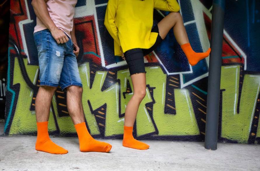 Two people standing next to a mural wearing bright orange Rainbow socks.