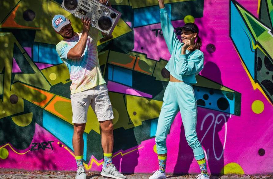 Mężczyzna i kobieta na tle muralu z odtwarzaczem radiowym w imprezowych skarpetkach Rainbow Socks.
