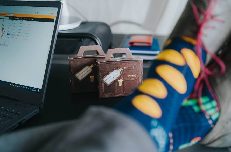 A laptop, two packages in the form of briefcases and a man’s feet in Rainbow cryptosocks.