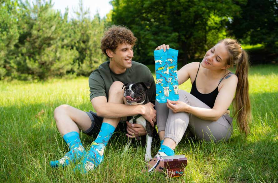 A man and a woman in dog socks on a meadow with a dog between them