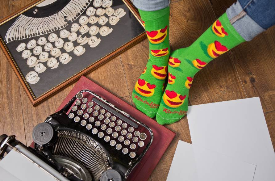 Osoba na podłodze z retro maszyną do pisania w skarpetkach z emotikonami od Rainbow Socks