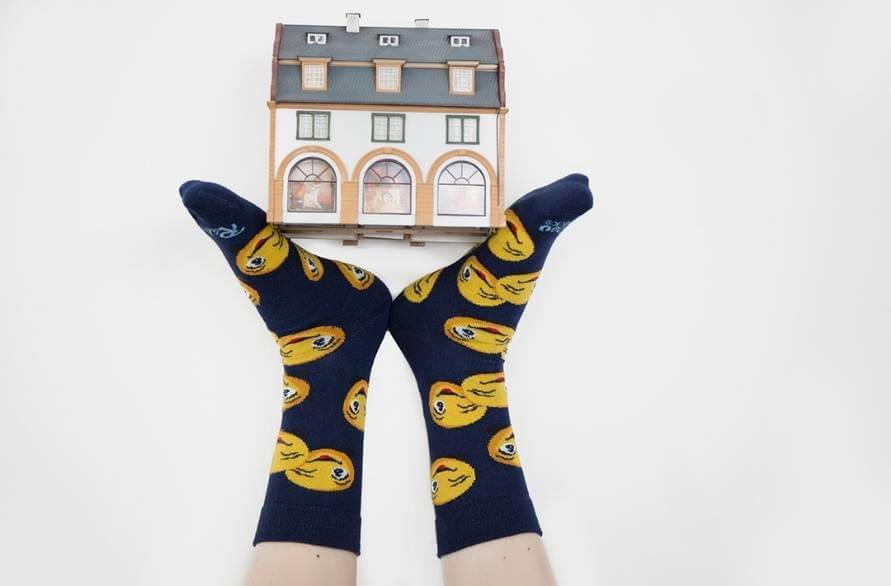 Feet in dark blue Emoji Socks with smiley emojis balancing a toy house