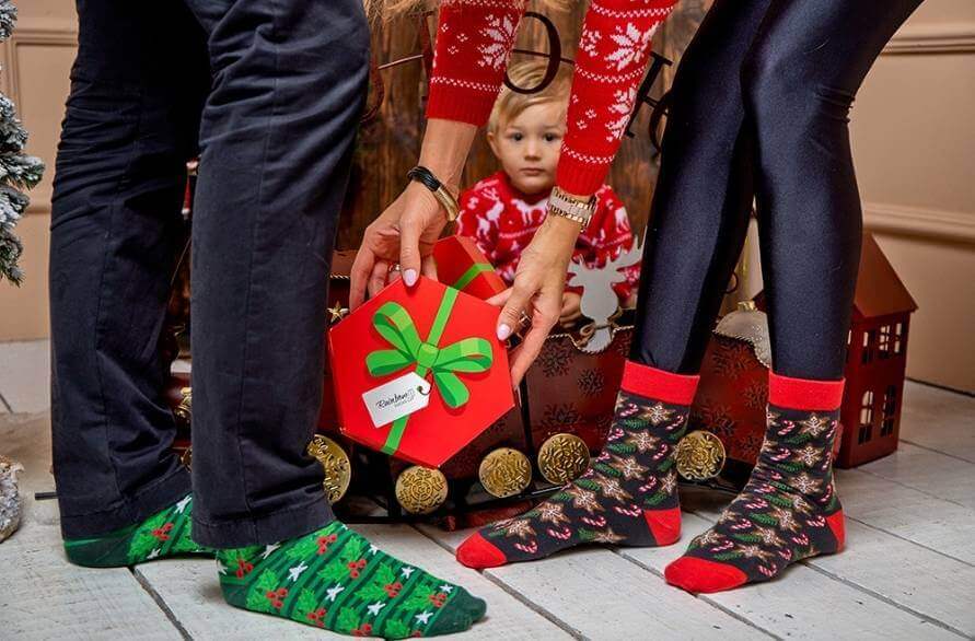 A little boy in a Christmas sweater and two adults wearing Rainbow Christmas Socks.  