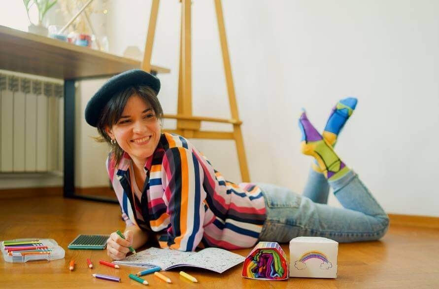 Kobieta leżąca na podłodze, kolorująca kredkami w skarpetkach Rainbow Socks.
