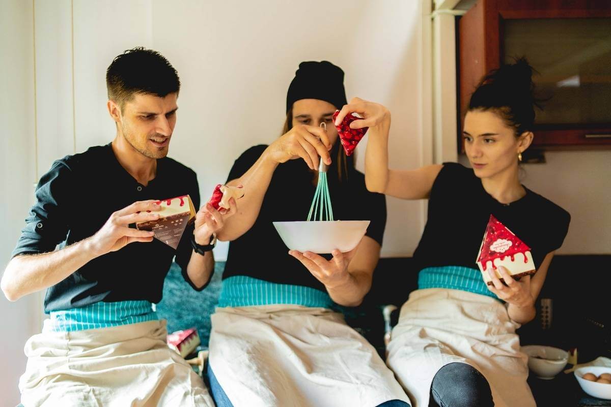 Three people making a cake with the cheesecake socks by Rainbow Socks in their hands.