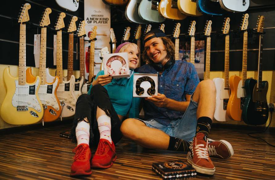Dwoje ludzi w sklepie muzycznym, w otoczeniu gitar, z dwoma zestawami słuchawkowych skarpetek.