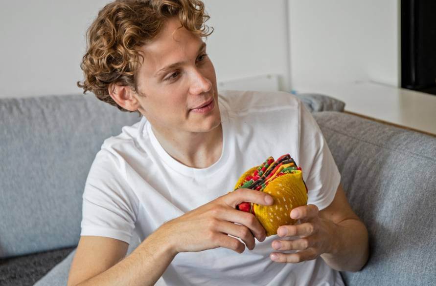 Mężczyzna na kanapie trzymający w rękach parę burgerowych skarpetek Rainbow Socks