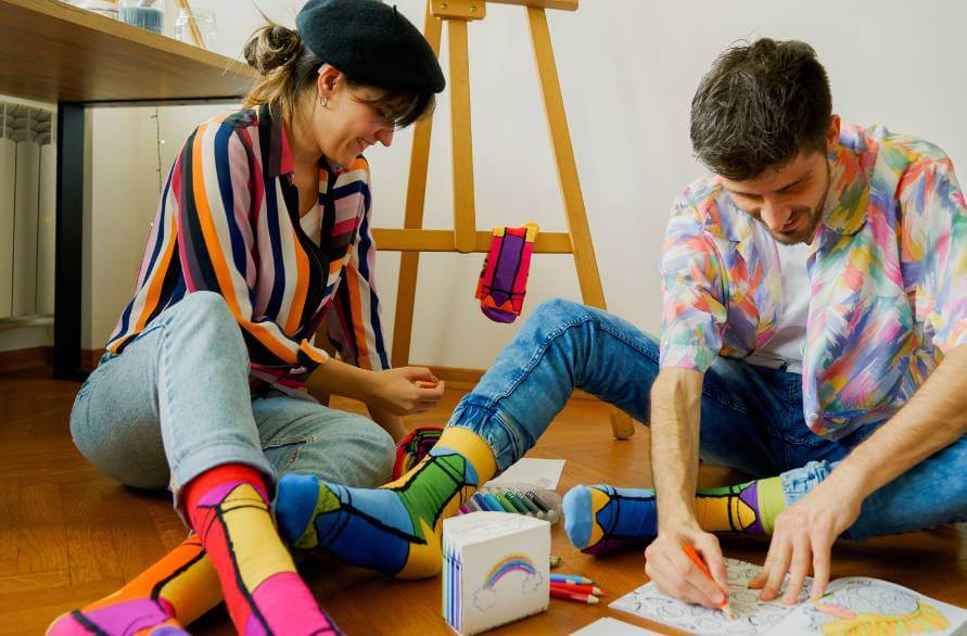 A woman and a man sitting on the ground and drawing, wearing Rainbow Socks.