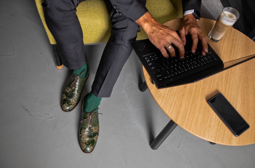 A man in a suit and green Rainbow Socks beside a coffee table with a laptop.