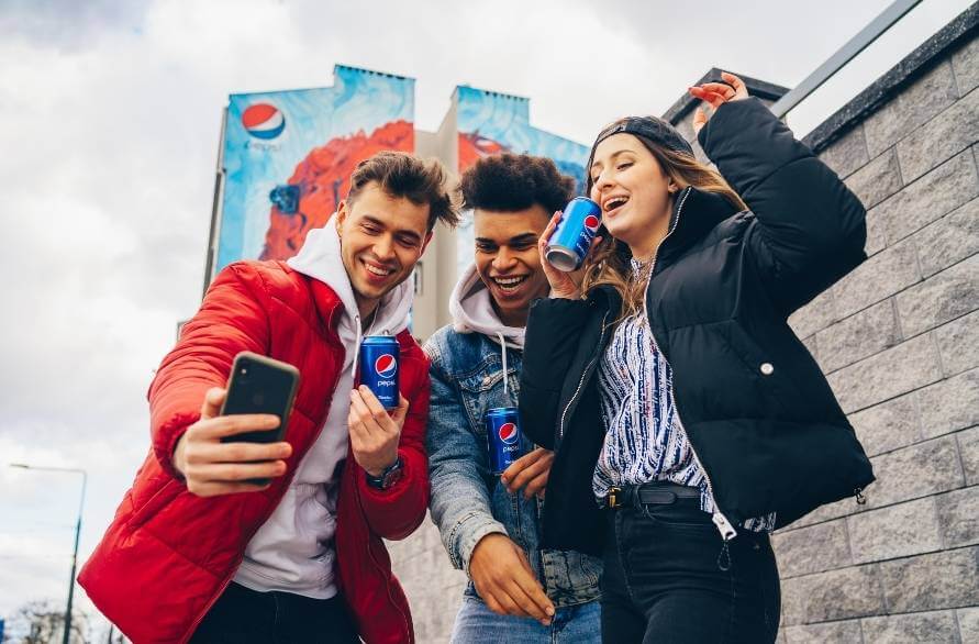 Troje młodych ludzi robi sobie wspólne zdjęcia w mieście ze skarpetkami Pepsi w puszce.