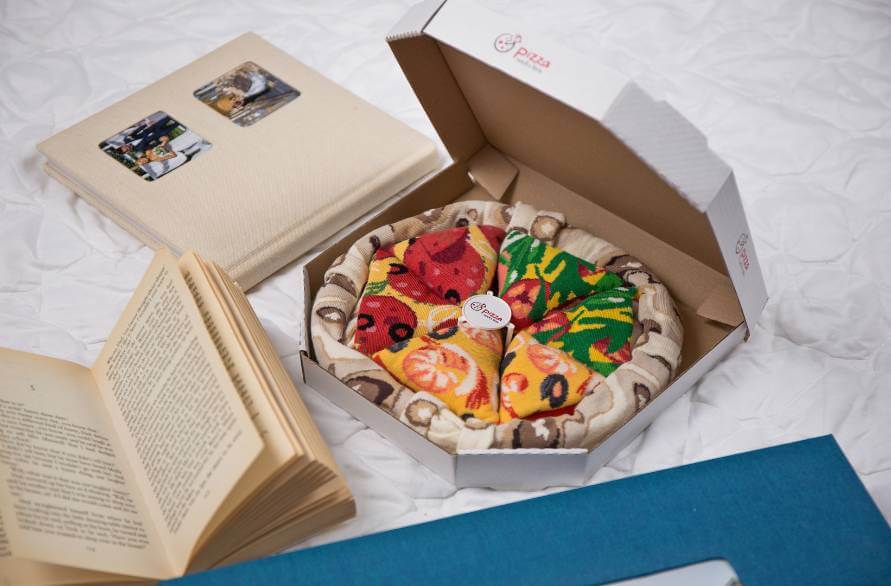 A pizza box with socks shaped into pizza slices next to a book and a photo album.