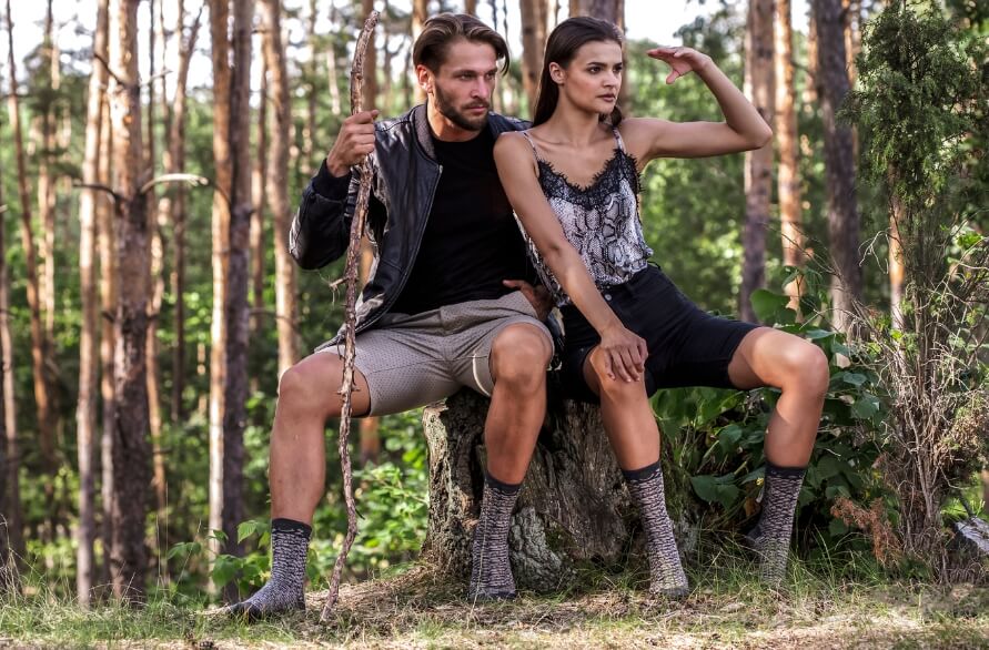 A man and a woman in a forest, sitting on a tree trunk, wearing reptile socks