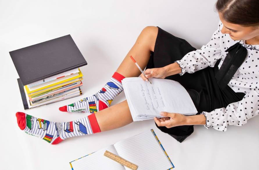 A woman sitting on the ground with Rainbow school socks on, studying