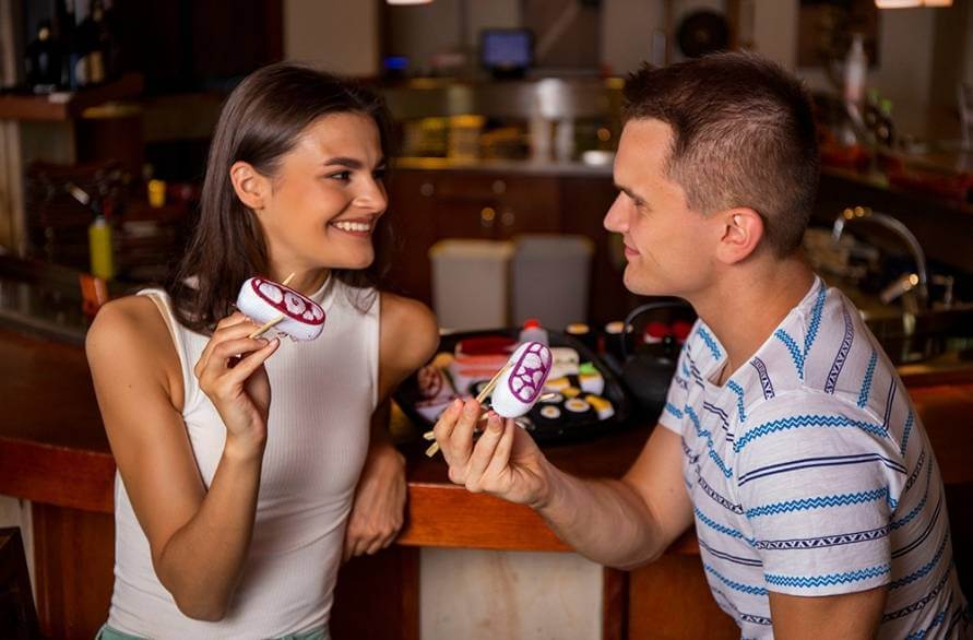 A woman and a man in a restaurant holding the chopsticks and a Rainbow Sushi Set.