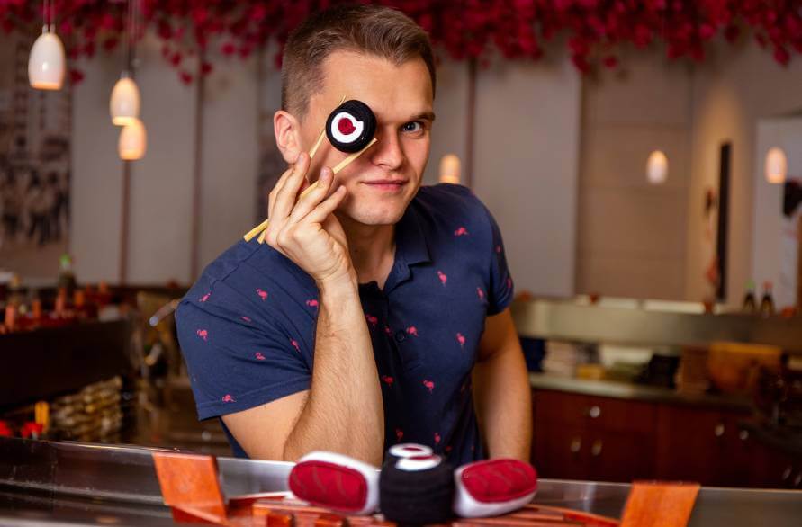 A man holding a sushi sock with chopsticks next to his eye.