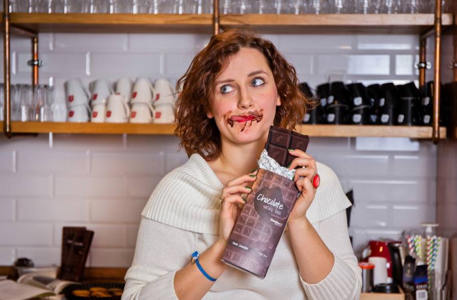 Kobieta w kuchni w czekoladowymi skarpetkami Rainbow Socks w ręce, ubrudzona czekoladą na twarzy.