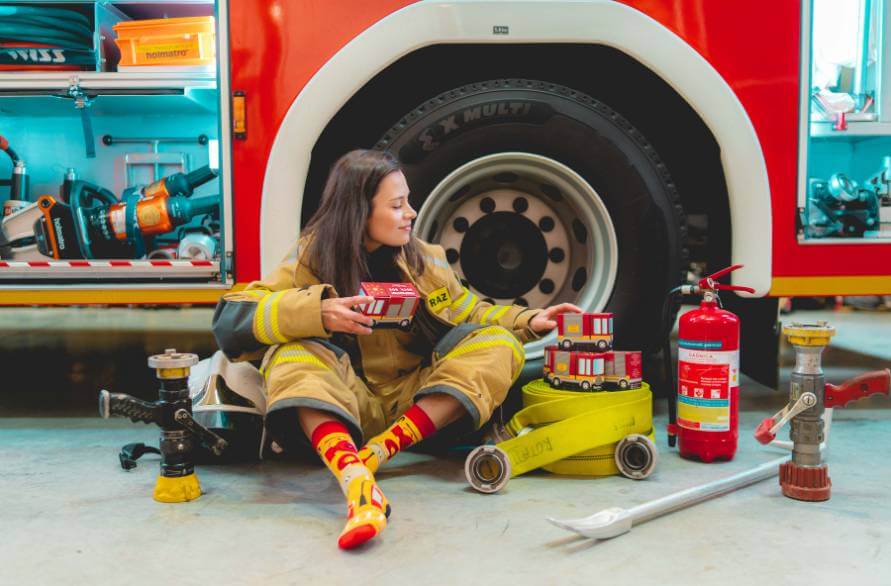A female firefighter sitting next to a fire truck with four boxes of firefighter socks and one pair on