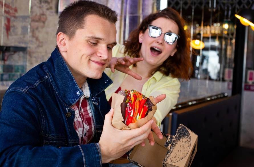 Mężczyzna trzyma skarpetki hamburgera Rainbow Socks, a kobieta obok próbuje je odebrać.