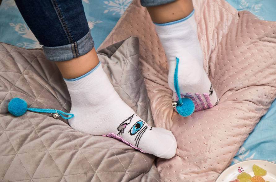 Feet of a person wearing white cat socks with blue pom-poms